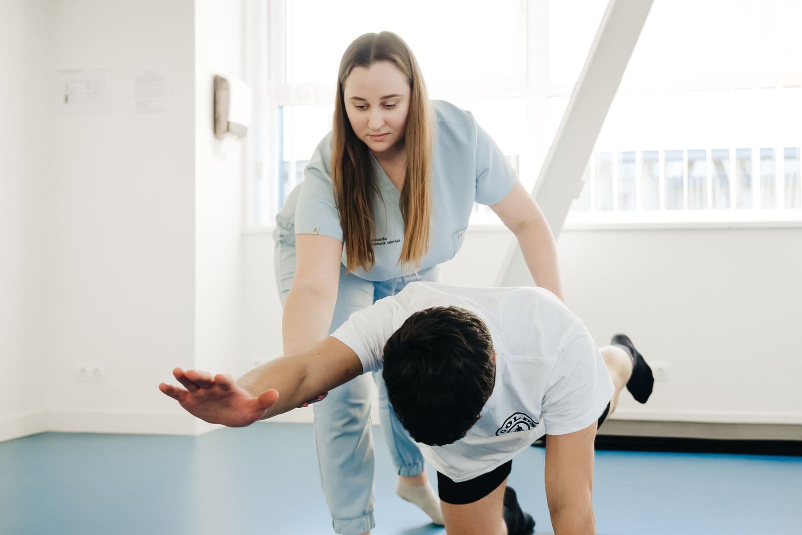 Specialistė veda klientą per judesio pratimą Alfa Steps klinikoje